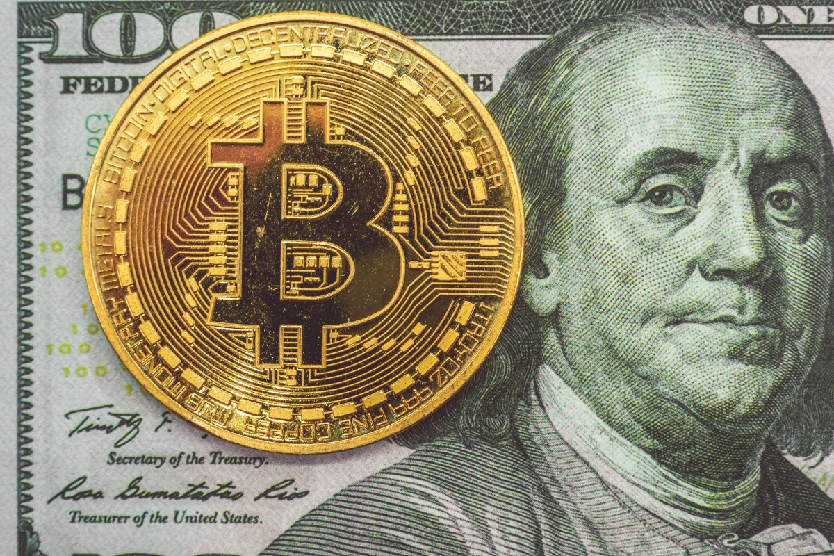 A bitcoin in front of a $100 bill. Depicting that crypto isn't money
