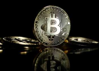 Picture of a standing bitcoin with two bitcoins lying on either side of it, with a black background