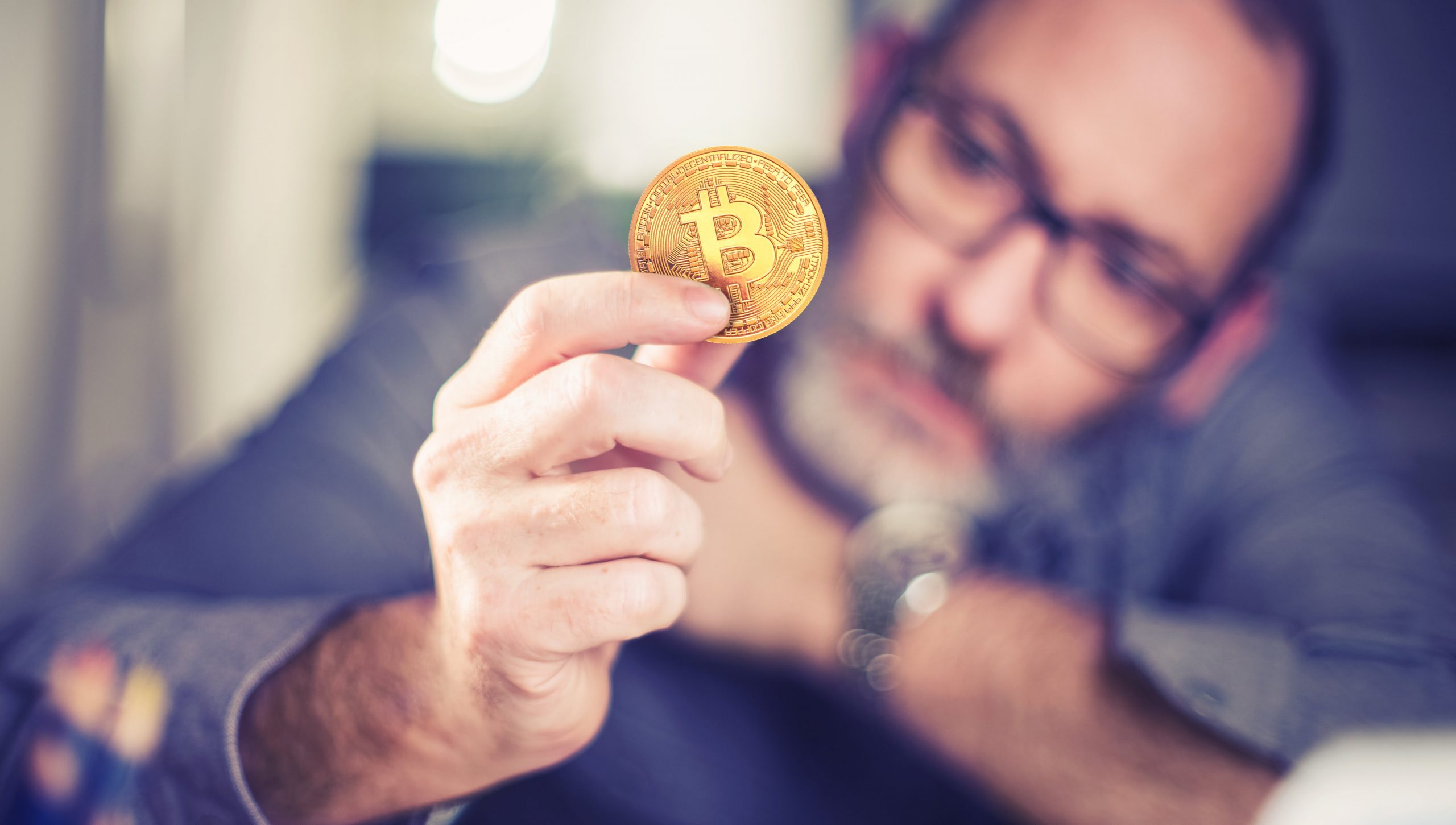 Picture of a man holding a bitcoin with a contemplative look on his face
