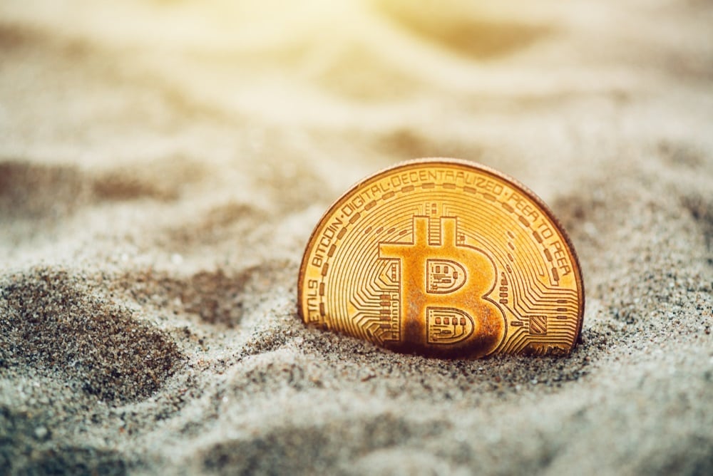 Picture of a bitcoin half-hidden in sand