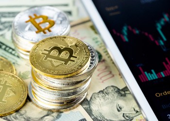 Picture of silver and gold bitcoins stacked together on top of a dollar bill