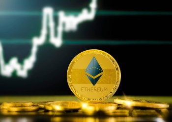 Picture of a gold Ethereum coin standing in front of an upward moving chart