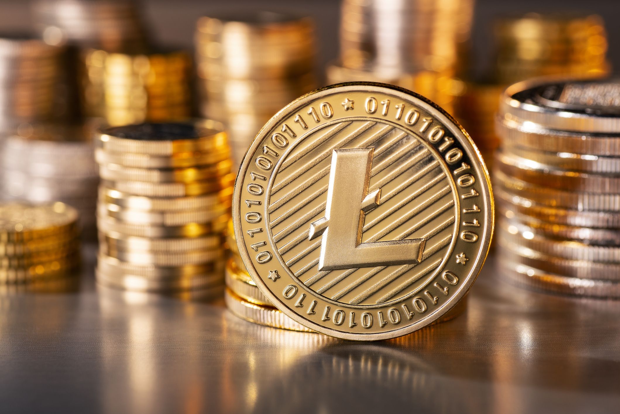 Picture of a gold Litecoin standing in front of stacks of other gold Litecoins