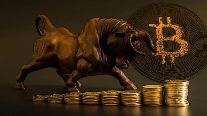 Picture of a bronze bull standing on stacked coins with a bitcoin next to it