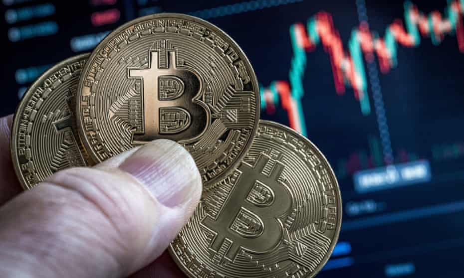 Picture of a hand holding three bitcoins with a market chart in the background