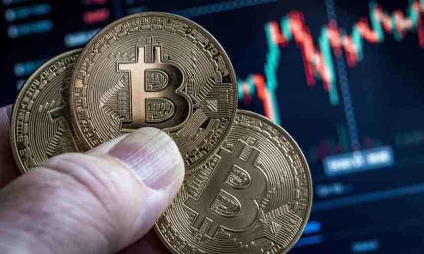 Picture of a hand holding three bitcoins with a market chart in the background