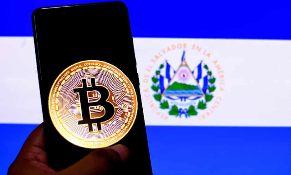 Picture of a Bitcoin logo on a smartphone in front of a flag of El Salvador