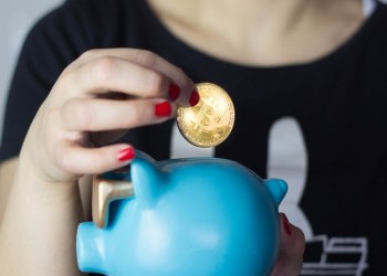Picture of a hand putting a bitcoin in a piggybank