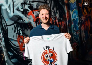 Martin Masser, ChangeNOW’s Director of Strategic Partnerships, holds a branded T-shirt in a graffiti-covered London passage.