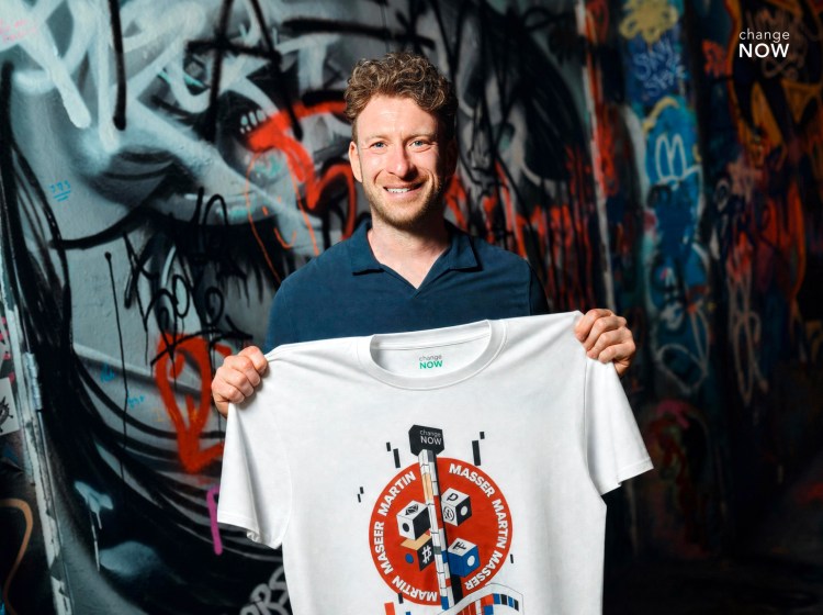 Martin Masser, ChangeNOW’s Director of Strategic Partnerships, holds a branded T-shirt in a graffiti-covered London passage.